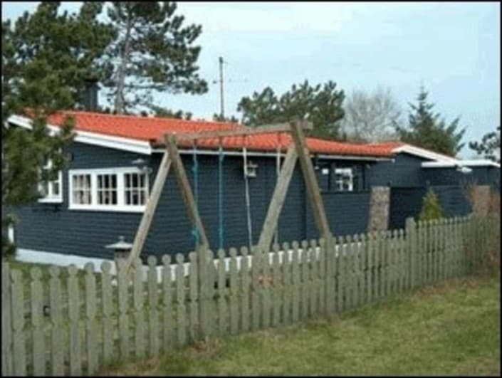 Sort hus med rødt tegltag og gynge i forgrunden